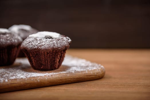 chocolate muffins with white icing lying on a Board sprinkled with powdered sugar