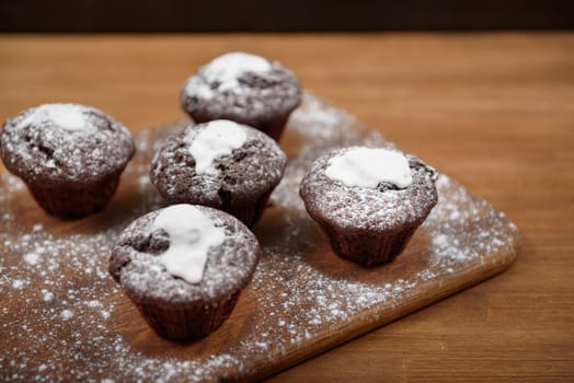 chocolate muffins with white icing lying on a Board sprinkled with powdered sugar