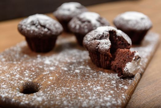 chocolate muffins with white icing lying on a Board sprinkled with powdered sugar