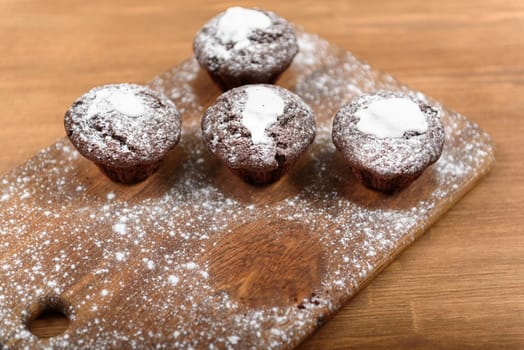 chocolate muffins with white icing lying on a Board sprinkled with powdered sugar