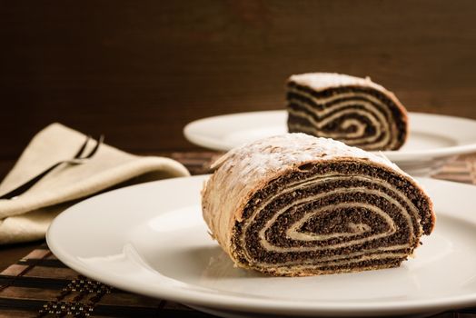 strudel with poppy seeds on a ceramic white plate on wooden background