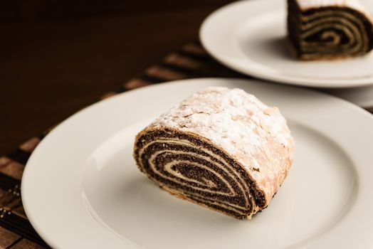 strudel with poppy seeds on a ceramic white plate on wooden background