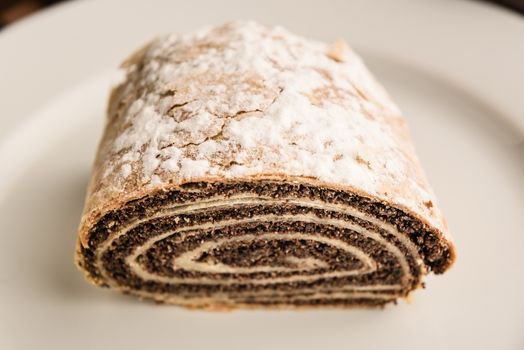 strudel with poppy seeds on a ceramic white plate on wooden background