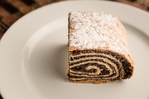 strudel with poppy seeds on a ceramic white plate on wooden background