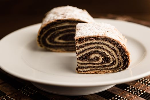 strudel with poppy seeds on a ceramic white plate on wooden background