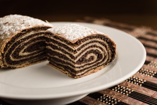 strudel with poppy seeds on a ceramic white plate on wooden background