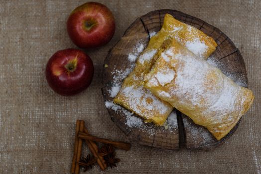 Apple strudel on wooden end of a tree with apples, cinnamon and star anise