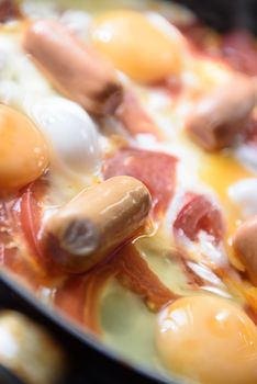 fried eggs with sausages and tomatoes on a hot pan, cooking breakfast