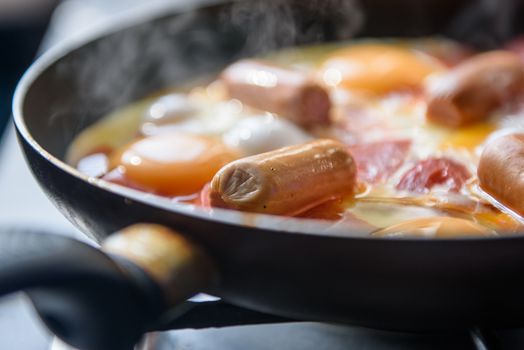 fried eggs with sausages and tomatoes on a hot pan, cooking breakfast