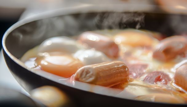 fried eggs with sausages and tomatoes on a hot pan, cooking breakfast