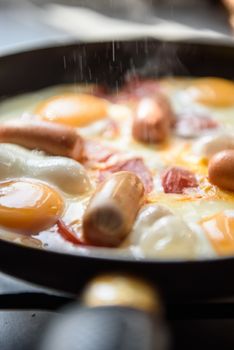 fried eggs with sausages and tomatoes on a hot pan, cooking breakfast