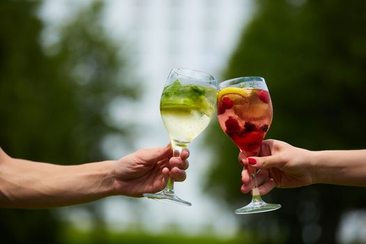 Hand holding glasses of cocktail clinking together at outdoor.