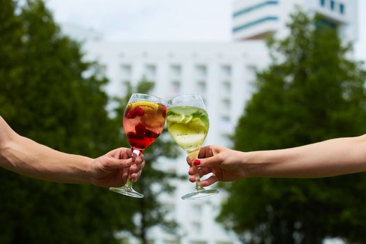 Hand holding glasses of cocktail clinking together at outdoor.