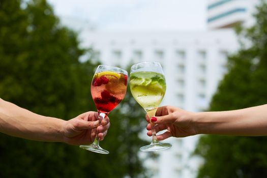 Hand holding glasses of cocktail clinking together at outdoor.