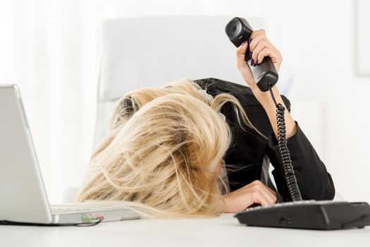 A young pretty businesswoman, exhausted from work sleeping in front of her laptop, leaning on office desk with a telephone handset on hand.