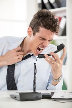Angry young Businessman sitting in the office and screaming on the phone