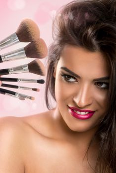 Portrait of a cute young brunette woman with set make-up brushes.