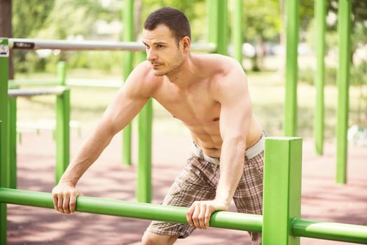 Naked muscle man resting after exercising in the outdoor gym.