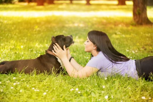 Beautiful young woman with her cute stafford terrier lying on grass in the park.