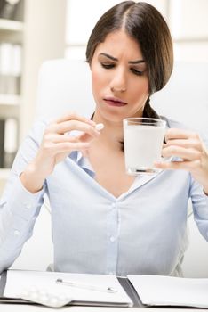 Young beautiful woman takes a pill in the workplace, in the background you can see the shelves with binders.