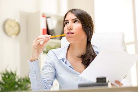 Portrait of a beautiful young businesswoman sitting in the office, biting pen and thinking.