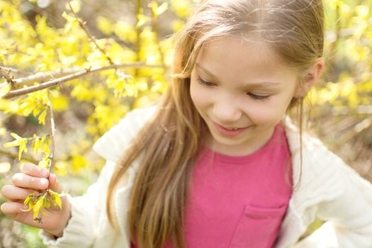 Smiling cute little girl standing beside a flower tree in the park and thinking.