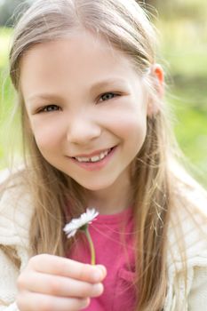 Smiling cute little girl in the park holding white flower and looking at camera.