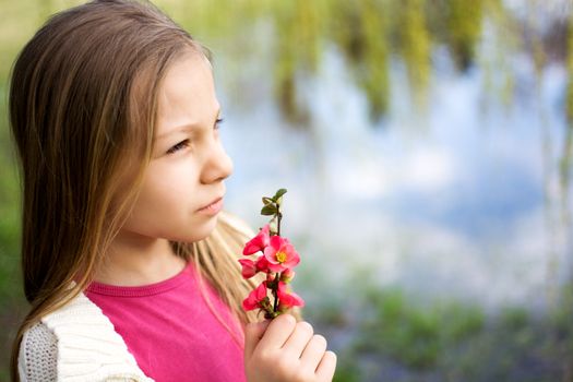 Beautiful little girl holding spring flower in the park and thinking.
