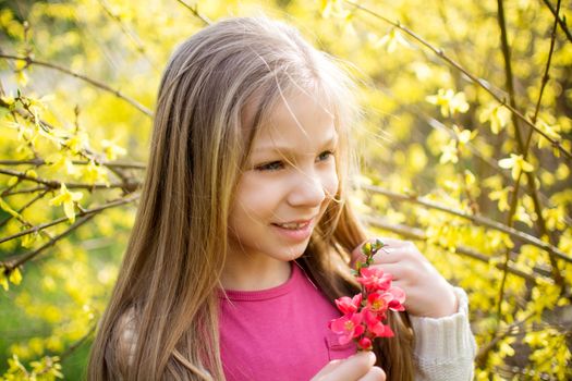 Smiling little girl smelling spring flower in the park and looking to the side.