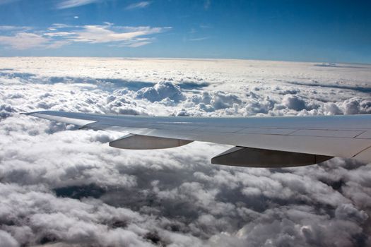 Airplane wing flying above white clouds.