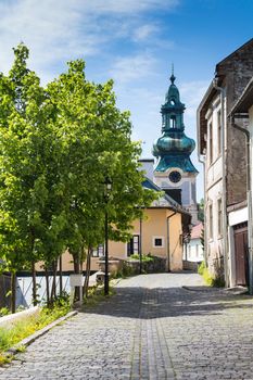 Small street on a hill in the medieval city Banska Stiavnica, Slovakia. Old houses and a tower of a church. Blue summer sky with some clouds.