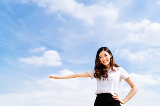 Beautiful young asian university or college student woman doing advertising or product presenting pose, copy space on blue sky background, education or job or advertisement concept