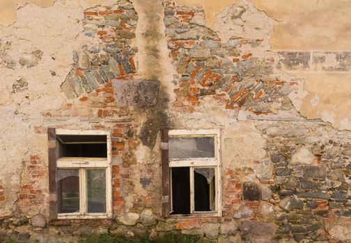 Couple of windows of an abandoned house. Broken glass. Wall of the building with many details of the colorful bricks and stones.