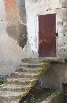 Concrete hanging staircase to the iron door of an old and abandoned house.