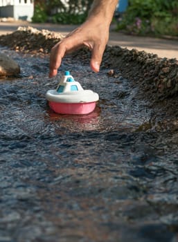 Close up of male hand holding plastic toy boat in the river stream. Playing the game.