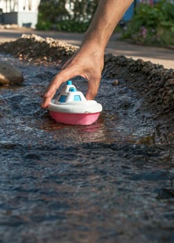 Close up of male hand holding plastic toy boat in the river stream. Playing the game.