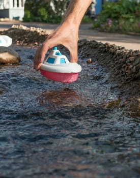 Close up of male hand holding plastic toy boat in the river stream. Playing the game.