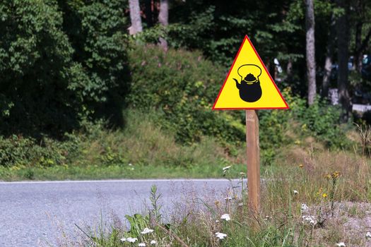 Yellow road sign with kettle or teapot on the side of the road.