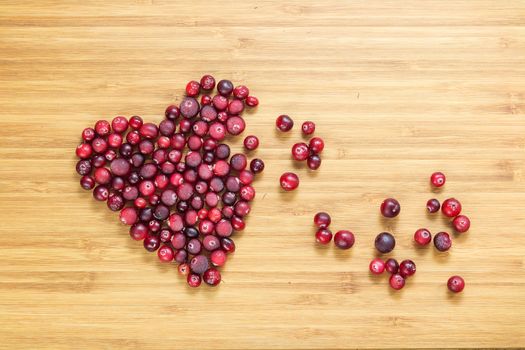 Cranberries in heart shape on wooden board with copy space, horizontal overhead view