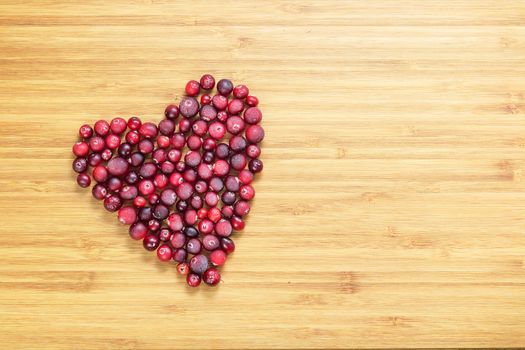 Cranberries in heart shape on wooden board with copy space, horizontal overhead view