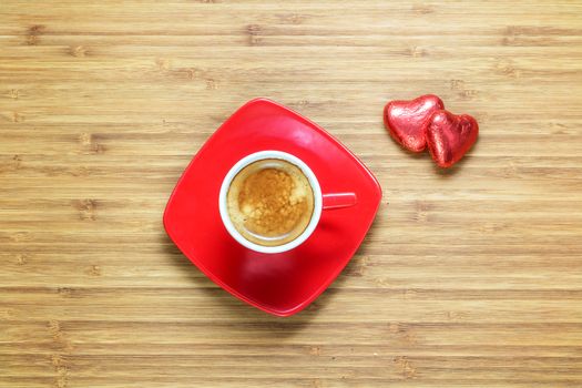 Heart shaped sweets wrapped in a bright red foil lying on a wooden texture with red cup of coffe near it. Background for romantic themes.