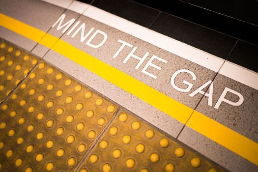 Mind the gap sign painted on train station's platform edge, conceptual, vignette darken edge, depth of field blur on far end