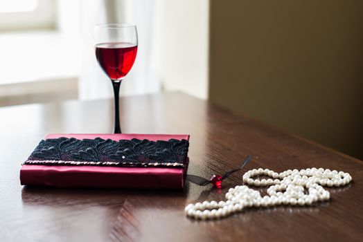 book decorated with maroon and white beads and a glass of red wine is on a brown table