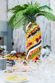 Palm tree decorated with exotic fruits on sticks stands on the wedding
