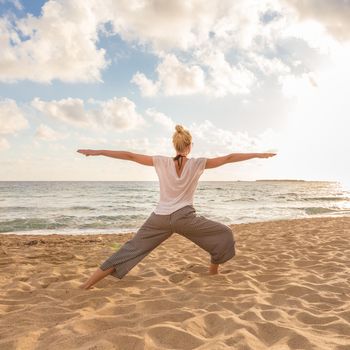 Active young woman practicing yoga on beach at sunset.