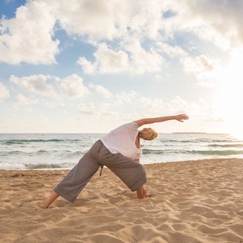 Active young woman practicing yoga on beach at sunset.