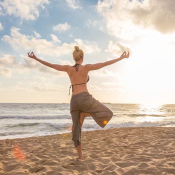 Active young woman practicing yoga on beach at sunset.