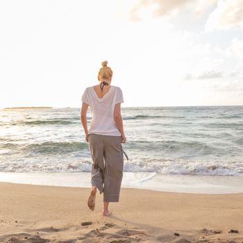 Woman walking on sand beach at golden hour. Seashore sunset walk.