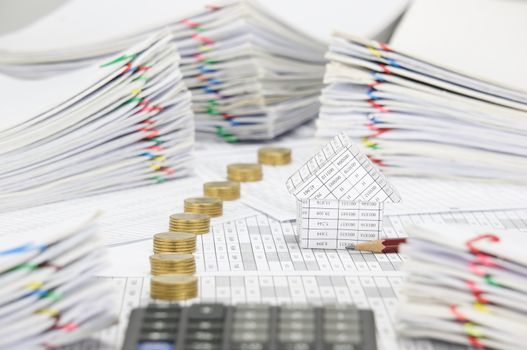 House and brown pencil on finance account have blur calculator and pile line of gold coins and pile overload paperwork of report and receipt with colorful paperclip place as foreground and background.