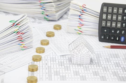 House and pile line of gold coins on finance account have blur brown pencil with calculator place vertical and pile overload paperwork of report and receipt with colorful paperclip place as background. 